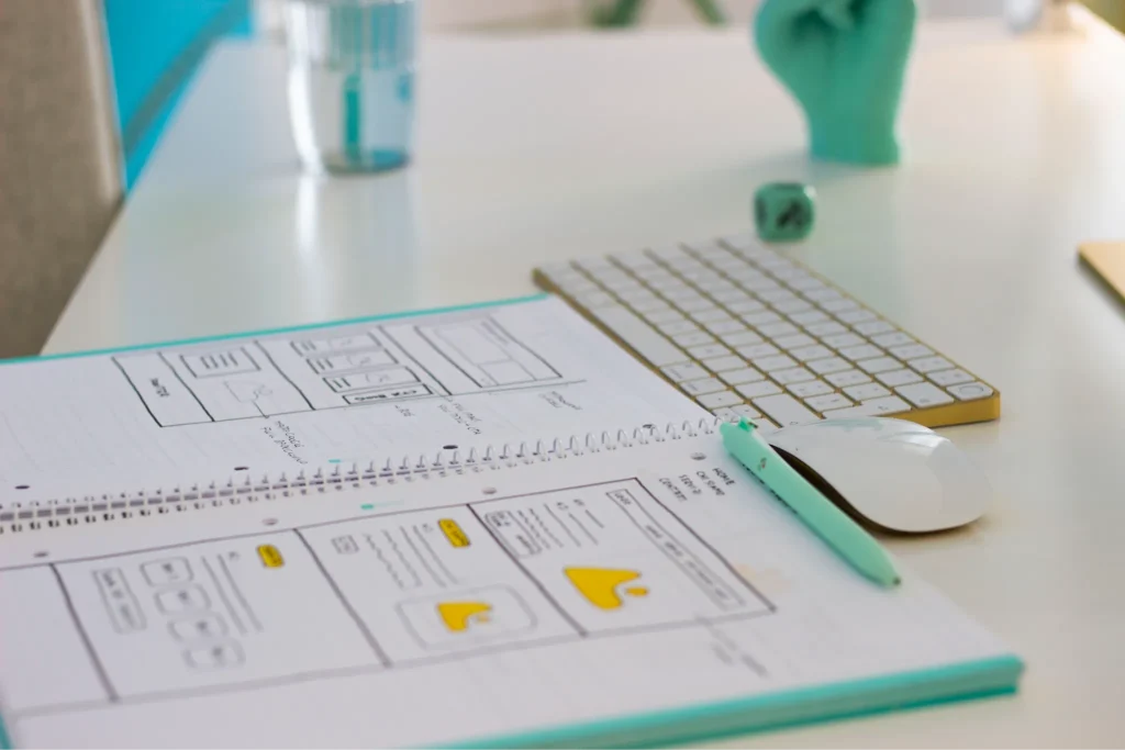 Wireframe di un sito web disegnati a mano su un quaderno, accanto a tastiera e mouse sulla scrivania